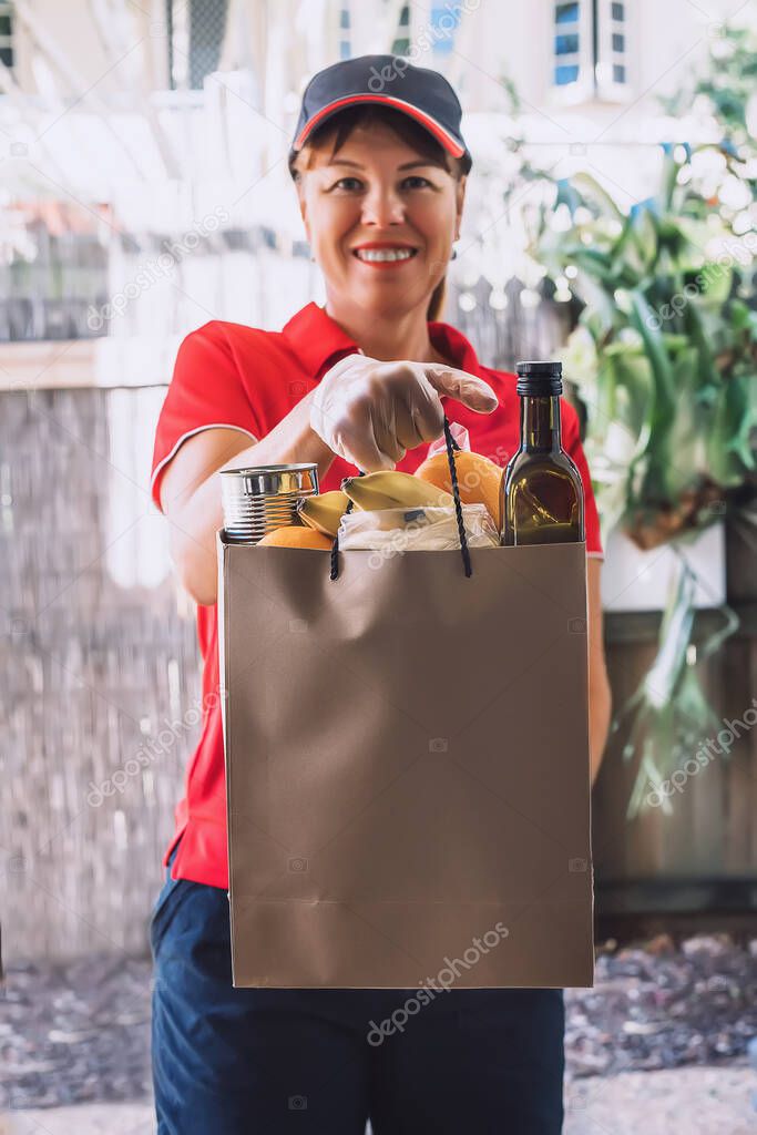 Delivery woman in protective gloves delivers paper bag with food products.
