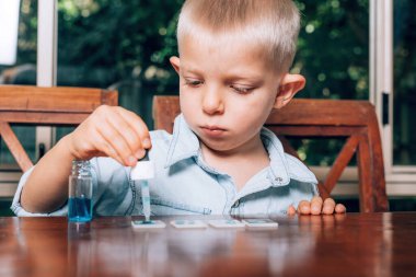 Küçük çocuk renkli su ve cam parçalarıyla deneysel laboratuvar aktivitesi yapıyor. Evde eğitim kavramı