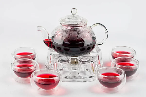 Chá vermelho em bule em stand com vela e copos de vidro no fundo branco — Fotografia de Stock