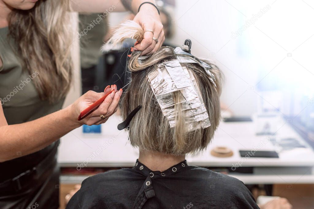 Master hairdresser in beauty salon coloring young womans hair using aluminum foil.