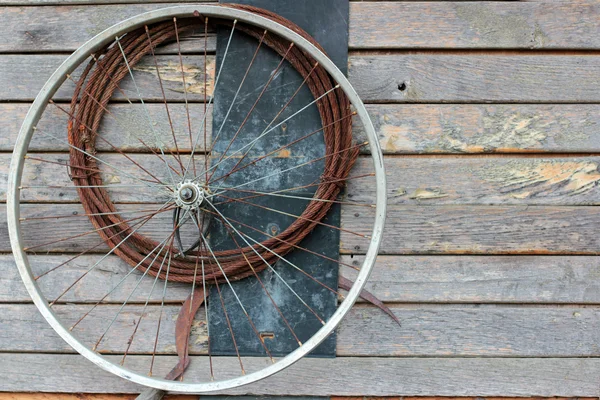 Old bike wheel and a rusty cable on a wooden wall — Stock Photo, Image