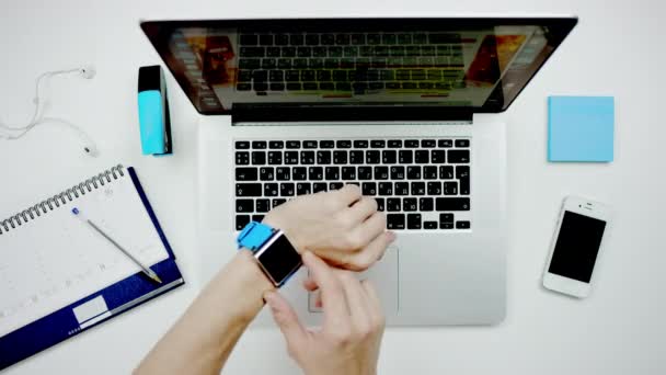 Человек смотрит на свои электронные часы на фоне ноутбука и стола — стоковое видео