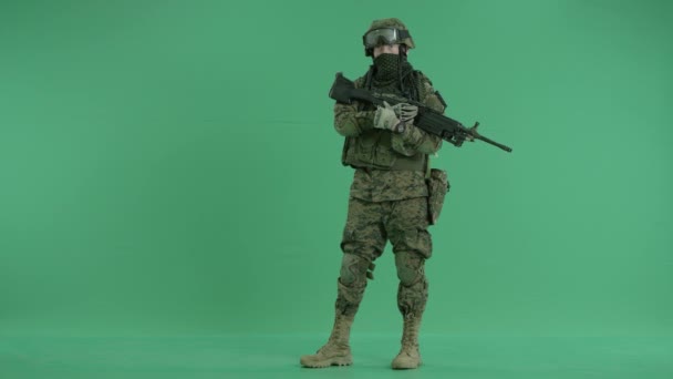 serviceman standing with weapon and looking at camera at green screen