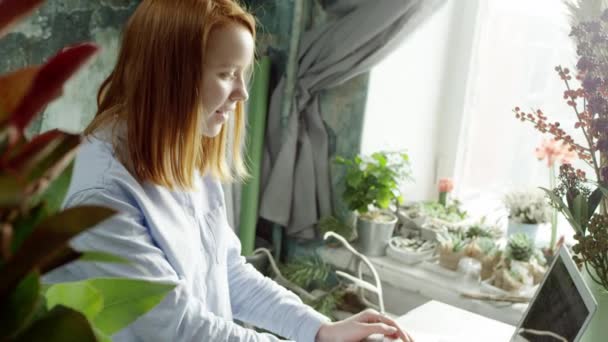 Florista de gengibre arranjando buquê e trabalhando com laptop — Vídeo de Stock