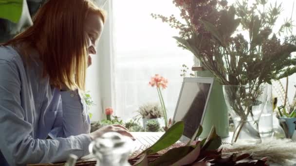 Vista lateral de floristería trabajando con portátil y sonriendo — Vídeos de Stock