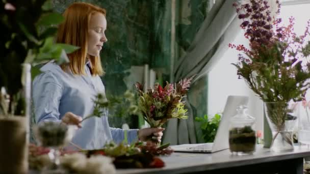 Lächelnder Blumenhändler arrangiert Blumenstrauß in der Nähe des Computers — Stockvideo
