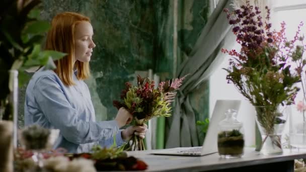 Ginger florist creaiting bouqet near table in office — Stock Video