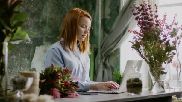 Floristería escribiendo en el ordenador portátil y sonriendo — Vídeo de stock