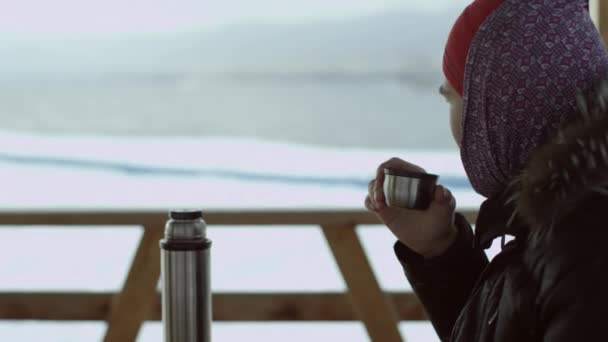 Homem bebendo chá de uma garrafa térmica na vista turva do lago — Vídeo de Stock