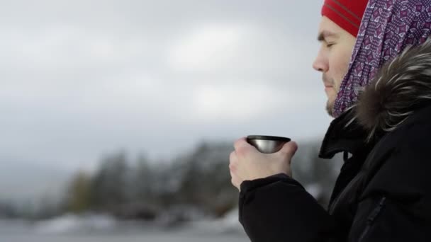 Man enjoying tea from a thermos at the view of winter lake — Stock Video