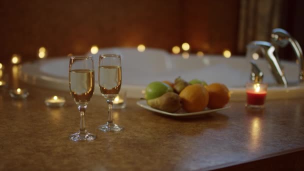 Plato con frutas y copas de champán de pie cerca del agua que fluye en el baño — Vídeos de Stock