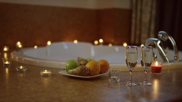 Vista de copas de champán y plato con frutas de pie cerca de jacuzzi en el baño . — Vídeos de Stock