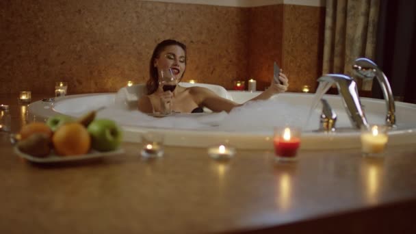 Sexig kvinna med rött vin i badet med skum tar selfie — Stockvideo