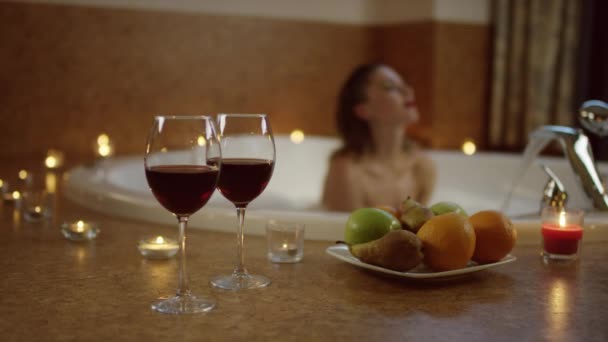 Sexy junge Frau entspannt sich im Schaum vor dem Hintergrund des romantischen Mittagessens mit Obst und Wein — Stockvideo