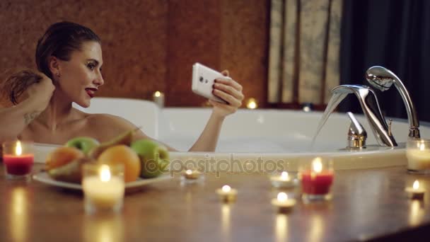 Женщина делает селфи в ванне с пеной в задней части романтического обеда — стоковое видео