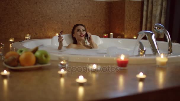 Smiling woman in bath with foam talking on phone and holding bank card. — Stock Video