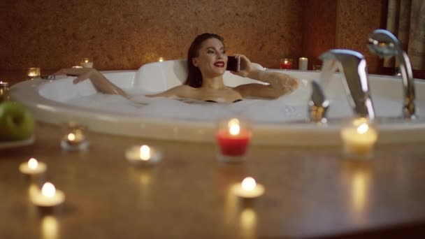Frau mit heller Kosmetik liegt in der Badewanne und telefoniert — Stockvideo