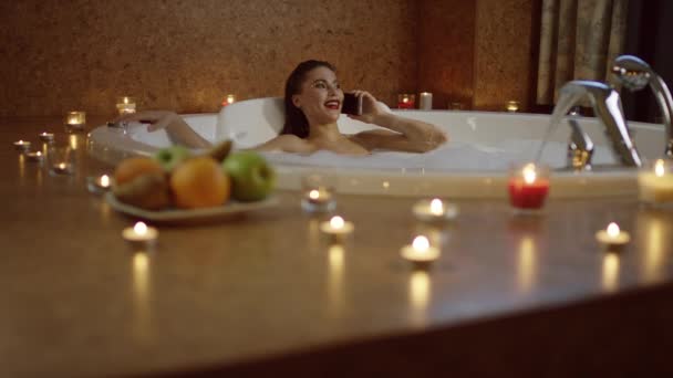 Smiling woman lying in bath and talking on phone — Stock Video