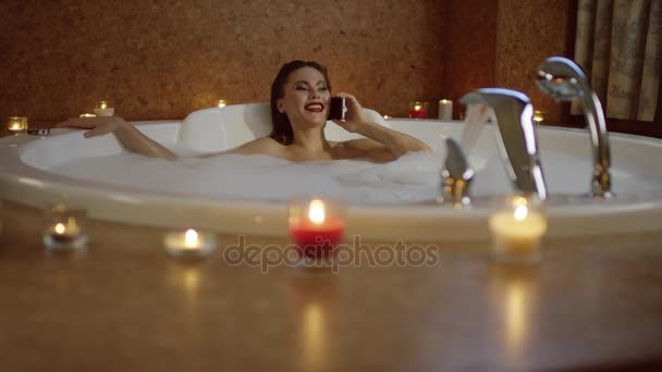 Vista desenfocada de la mujer acostada en el baño y hablando por teléfono — Vídeos de Stock