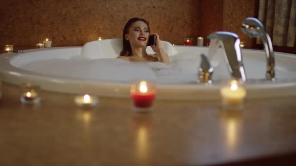 Дівчина з яскравою косметикою лежить у ванні і розмовляє по телефону — стокове відео