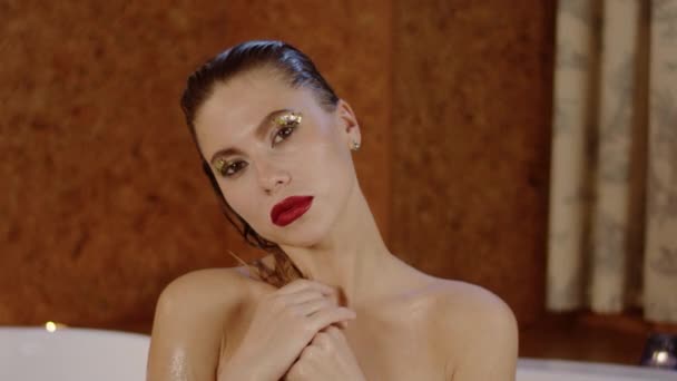 Сексуальна молода жінка з яскравою косметикою дивиться на камеру у ванній . — стокове відео