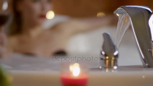 Femme avec le verre de vin rouge à l'arrière-plan flou de l'eau coulant dans le bain — Video