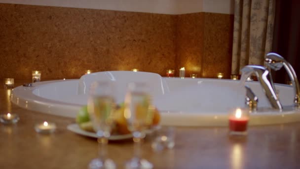 Vue des verres de champagne et assiette avec des fruits debout près du jacuzzi dans la salle de bain . — Video