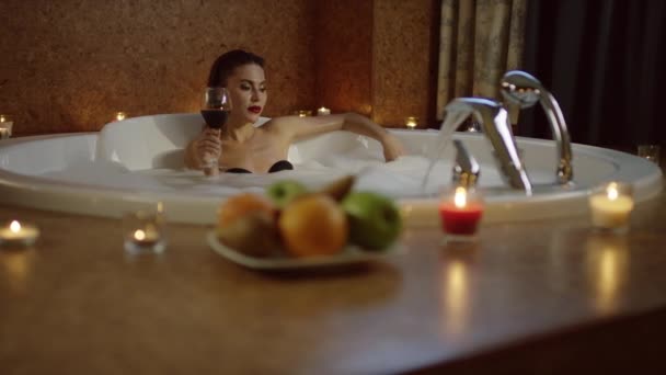 Μοναχική γυναίκα πίνοντας κόκκινο ποτό σε μπάνιο με αφρό — Αρχείο Βίντεο