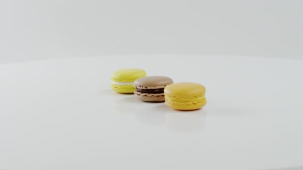 Three colourful macarons are rotating together on the white surface — Stock Video