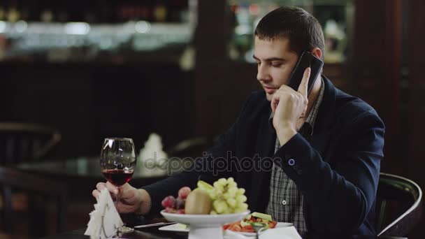 Handsome man talking on mobile phone in cafe and drinking wine — Stock Video