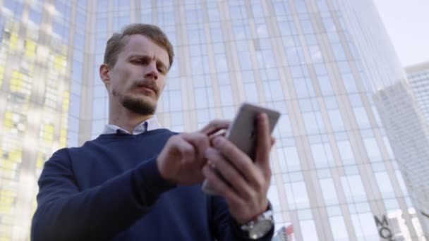 Hombre serio escribiendo mensaje en el teléfono inteligente en la ciudad — Vídeo de stock