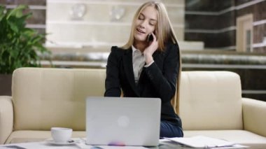 Dizüstü bilgisayar kullanarak ve cep telefonu bir lobisinde konuşurken kadın