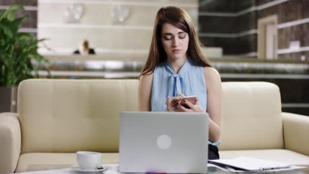 Nő használ laptop és mozgatható telefon-ban egy előcsarnok beszél — Stock videók