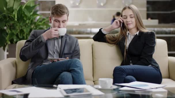 Muž s šálkem kávy a žena mluví o telefonu v hale — Stock video