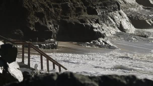 Морские волны врезаются в пляж и скалистые скалы, с близкого расстояния — стоковое видео