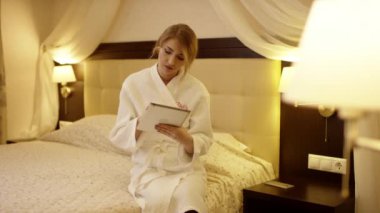 Genç güzel kadın yatakta oturur ve tablet bir şey üzerinden hareketleri