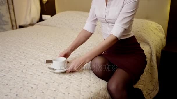 Mujer joven está sentada en la cama y bebiendo una taza de té — Vídeos de Stock