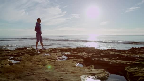 Guy está de pie en una orilla del mar y mirando un hermoso paisaje — Vídeos de Stock