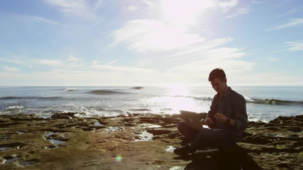 Glad attraktiv ung man på en strand med ett kreditkort och en bärbar dator är att köpa något över Internet — Stockvideo