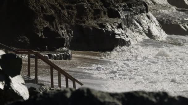 Океанічні хвилі врізаються в пляж і скелясті скелі — стокове відео