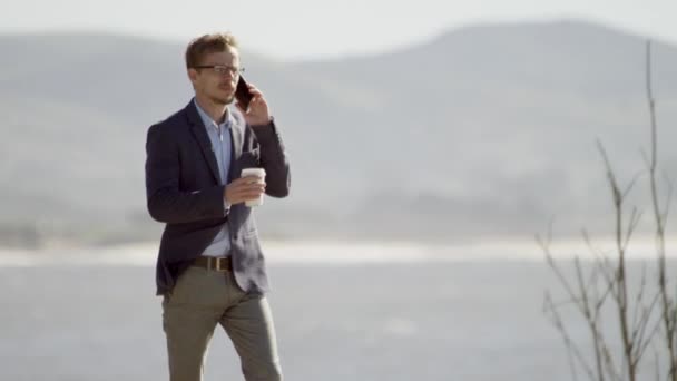 Joven hombre de negocios caminando por la costa del océano Pacífico — Vídeos de Stock