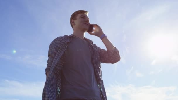 Netter junger Mann unterhält sich fröhlich über sein Smartphone auf der Straße — Stockvideo