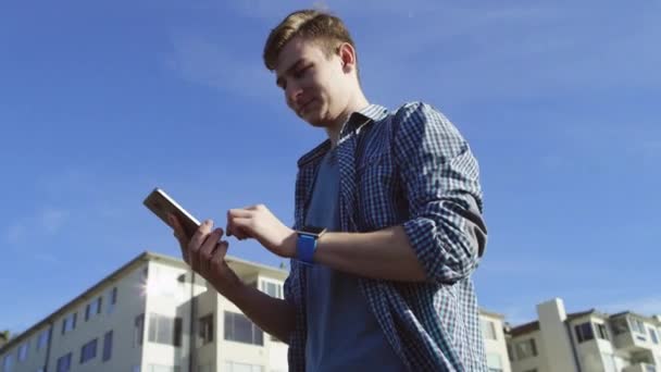 Attraente ragazzo sta usando il suo smartphone su una strada — Video Stock