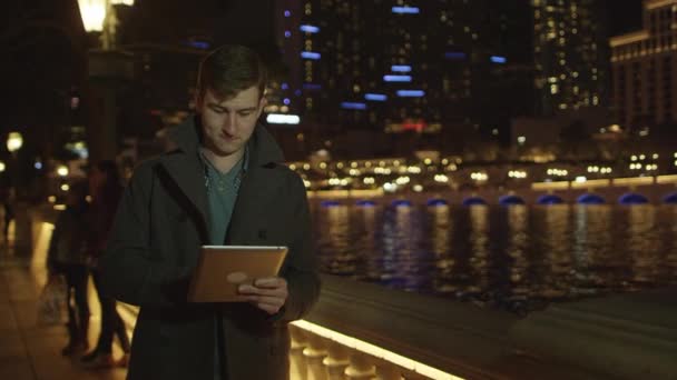 El joven está de pie cerca de la fuente con una tableta de PC — Vídeo de stock