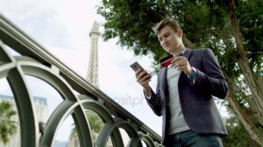 Çekici adam Eyfel Kulesi bir arka plan üzerinde onun smartphone ve bir kredi kartı kullanarak online alışveriş