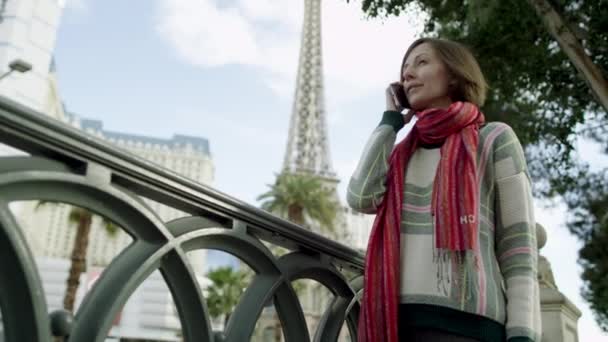 Ung vacker kvinna är att ha en telefon prata när du står på en trottoar i Las Vegas med Eiffeltornet på en bakgrund — Stockvideo