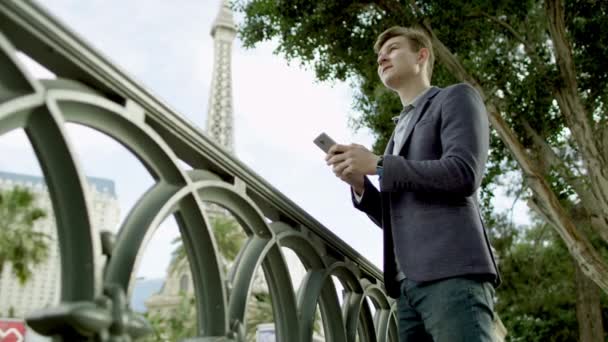 Knappe jongen is SMS via een smartphone met de Eiffeltoren op een achtergrond — Stockvideo