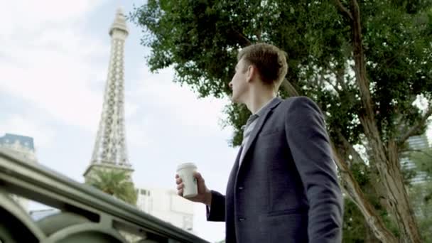 Un tipo atractivo está tomando café en una acera con la torre Eiffel sobre un fondo — Vídeo de stock