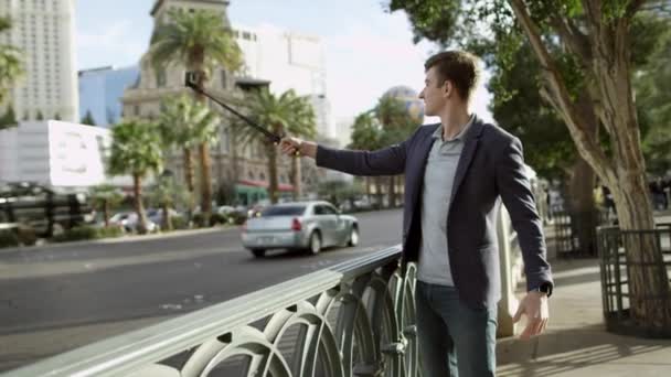 Young handsome is taking a selfie on a sidewalk by using a selfie stick and a smartphone — Stock Video