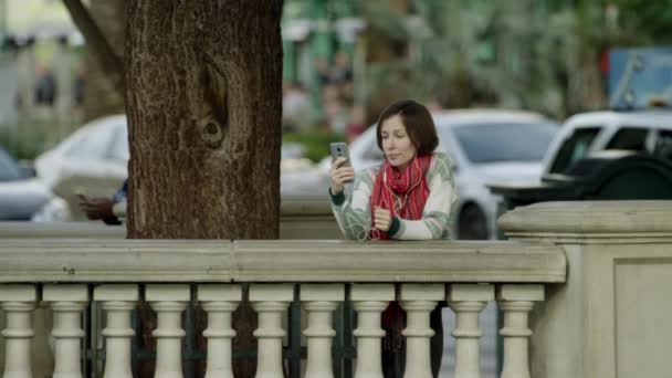 Mulher bonita nova está tendo um bate-papo de vídeo em uma calçada ao lado de uma árvore — Vídeo de Stock